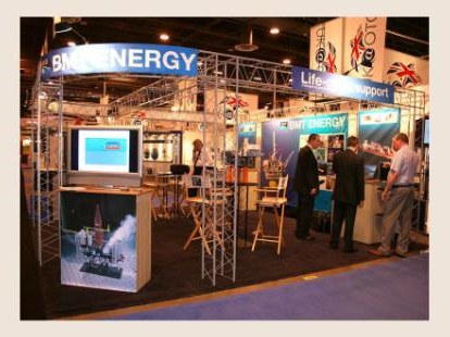 A trade show booth with BMT Energy signage, screens, and visitors