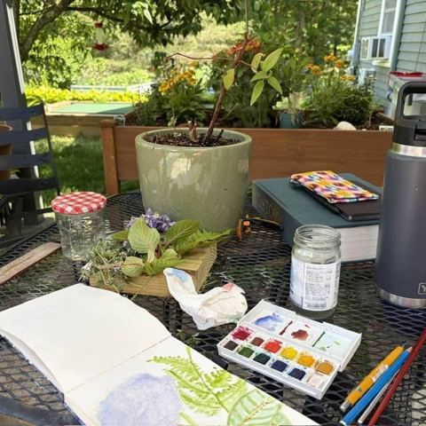 A watercolor sketchbook and paint box on a garden table